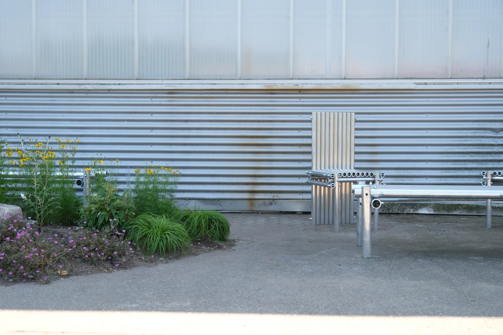 Tubular metal seating beside planting and the corrugated industrial facade